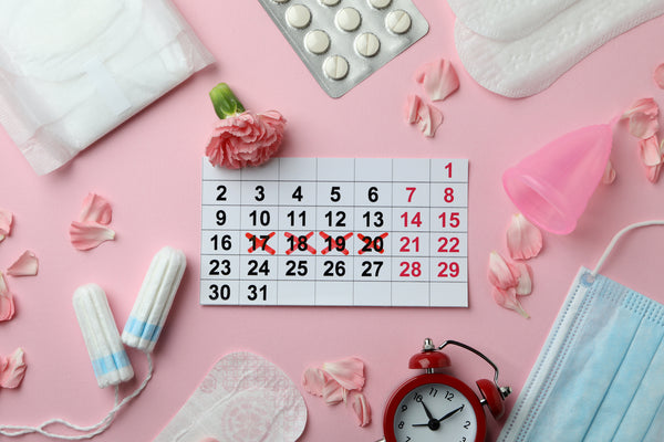 Period supplies like tampons, menstrual pads, calendar, face mask, menstrual cup, pills in blister pack, flowers, clock on pick background. 