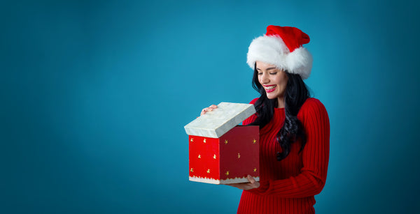 Young lady wearing a red sweater and a Christmas hat. She is grinning happily while opening her Christmas present.   