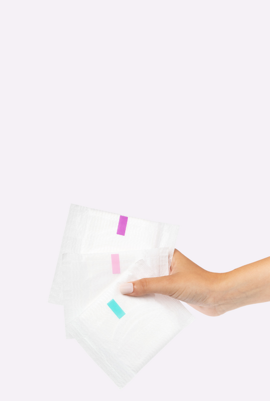 Woman holding three pads in wrapping with a light pink background