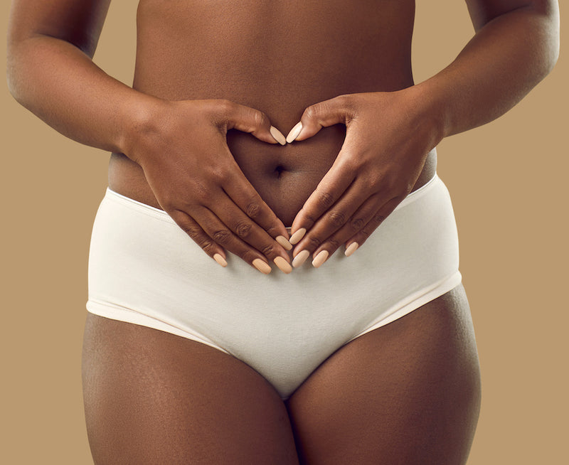 Woman holding her stomach with her hands in the shape of a heart with white underwear on 